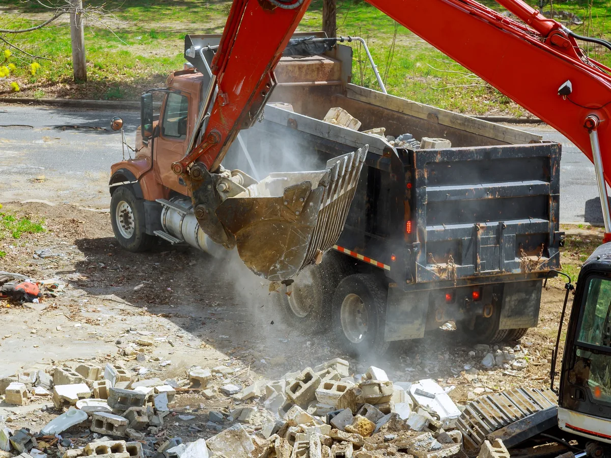 Excavator loading broken block and concrete into a dump truck on a past project