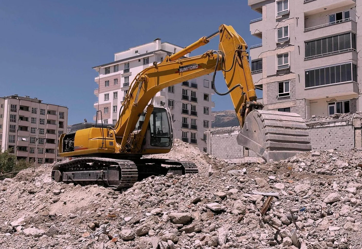 Excavator working on a pile of rubble beside a multi-story building