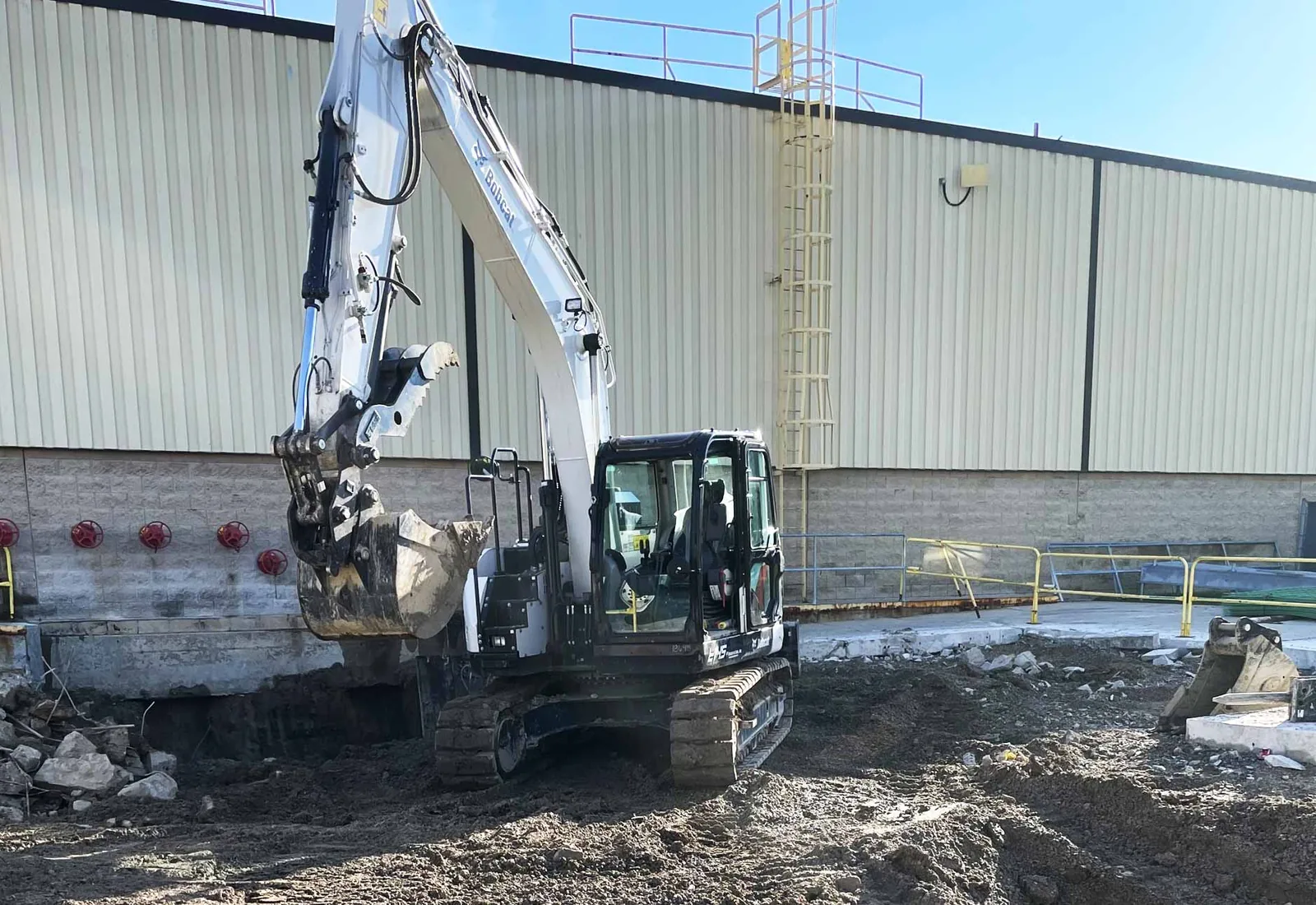 Excavator breaking out paving beside a commercial metal building