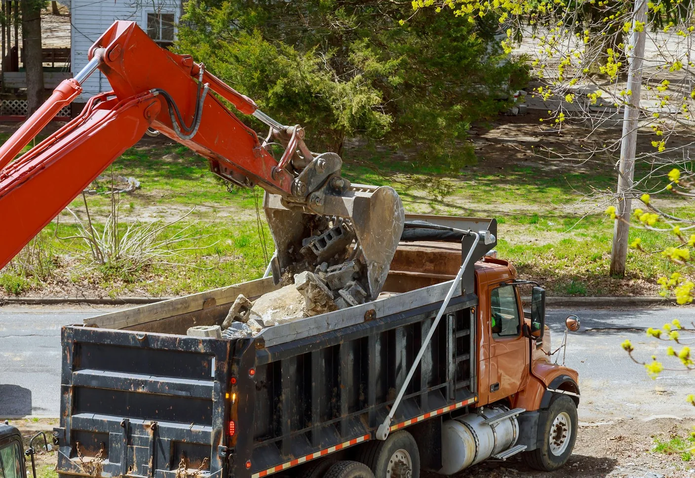 Excavator dropping broken concrete debris into a dump truck