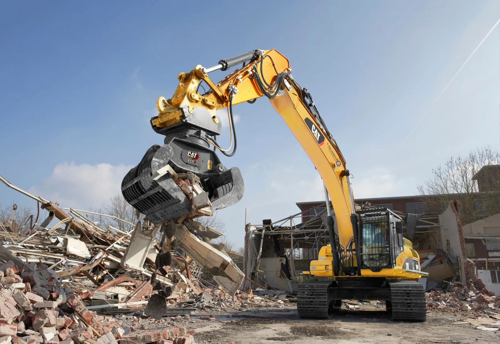 Excavator with a demolition grapple pulling apart a partly demolished building