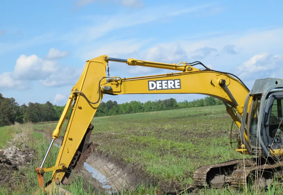Excavator shaping a drainage swale across an open field
