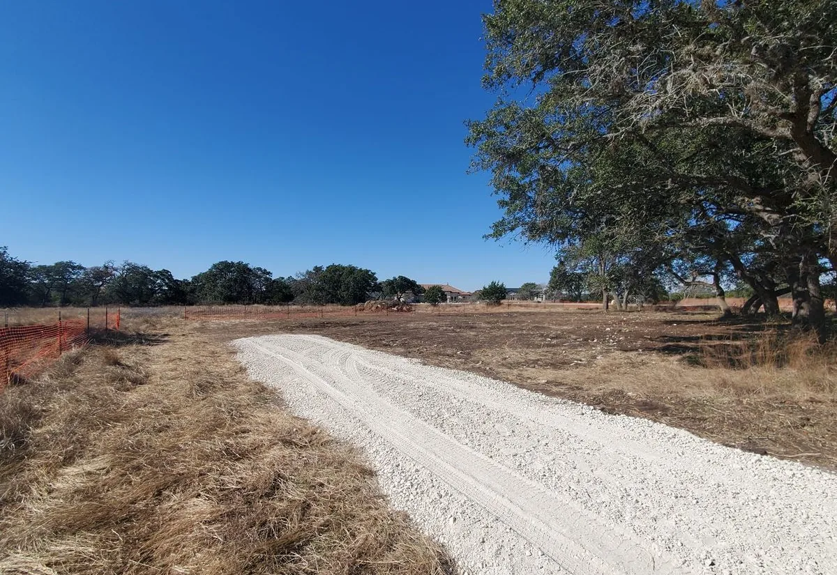 Fresh caliche drive graded across a cleared rural lot with live oaks