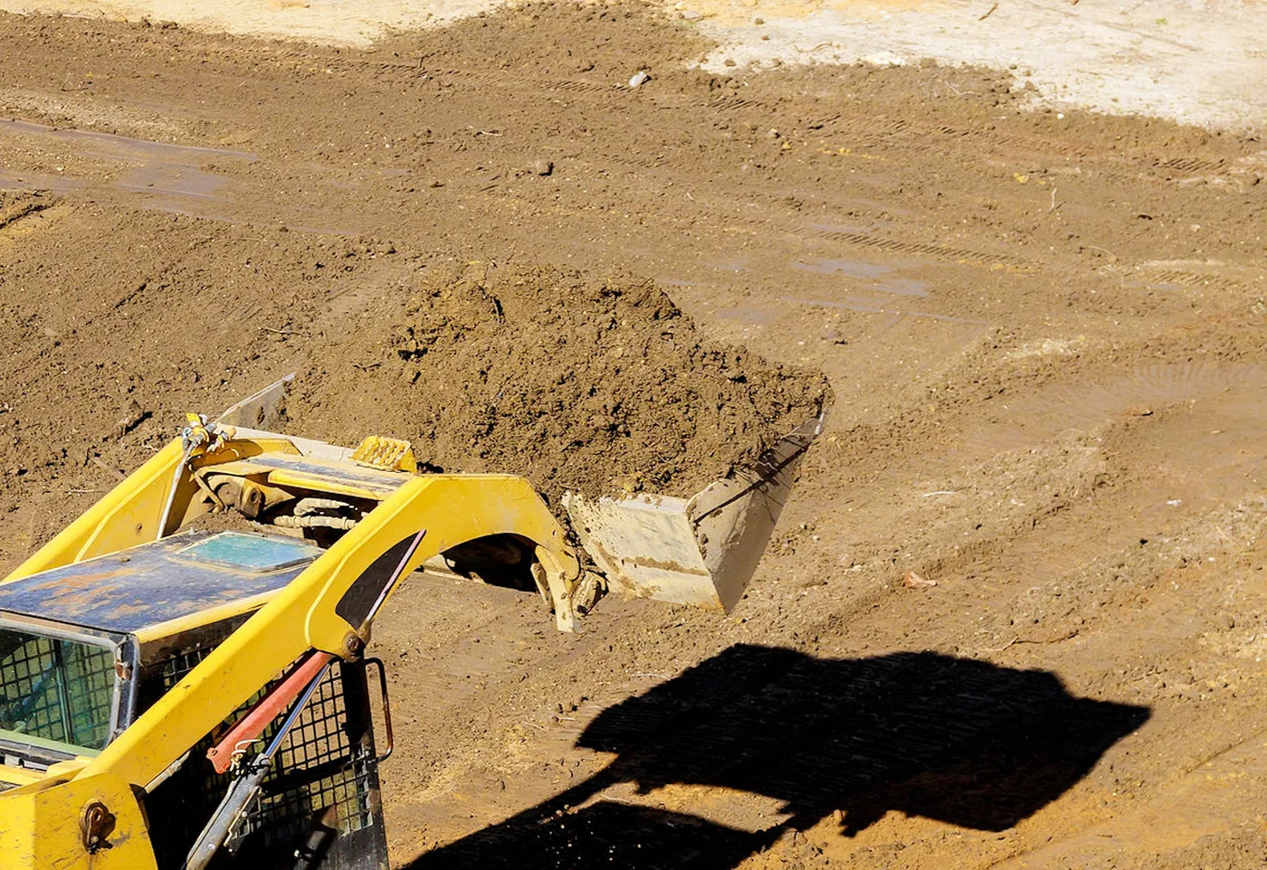 Track loader dumping a bucket of fill dirt while grading a lot