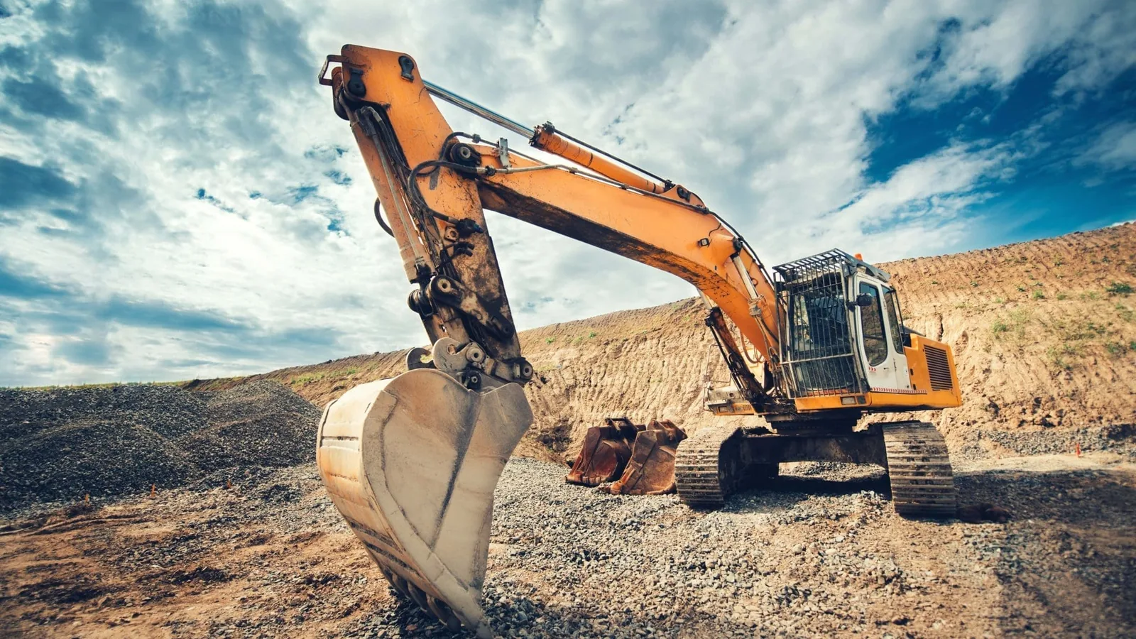 Excavator digging on an open dirt site under a heavy sky
