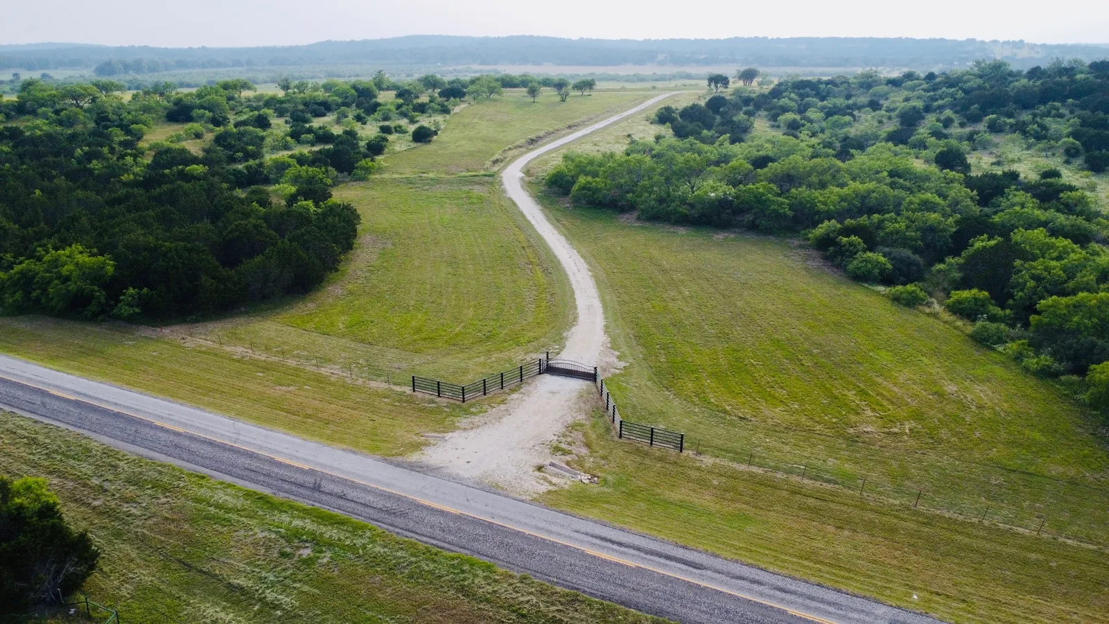 Aerial view of a caliche ranch drive running back from a gated county road