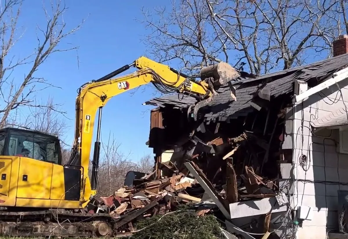 Excavator tearing into the roof of a single-family house