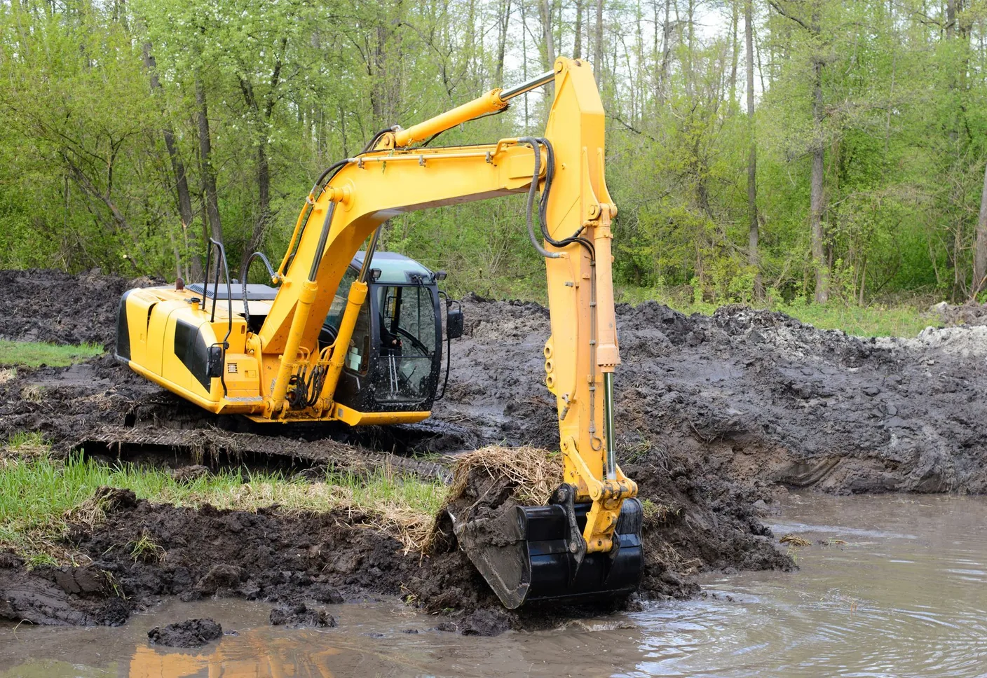 Excavator digging out a pond basin in wet ground