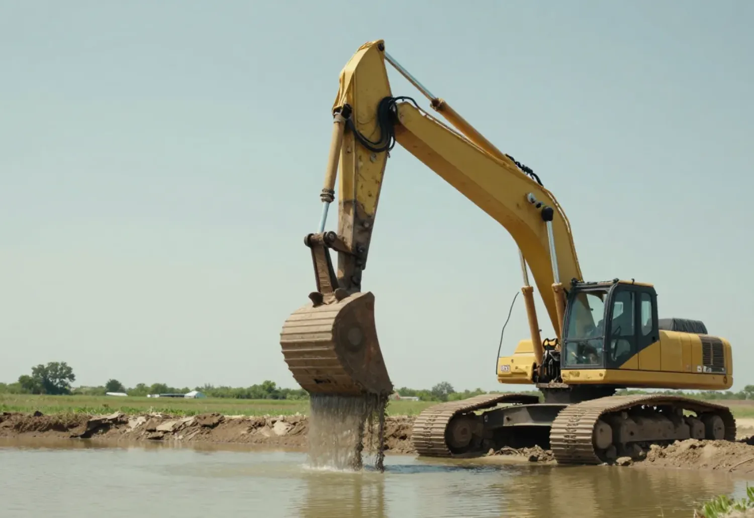Excavator working from the bank to clean silt out of a pond