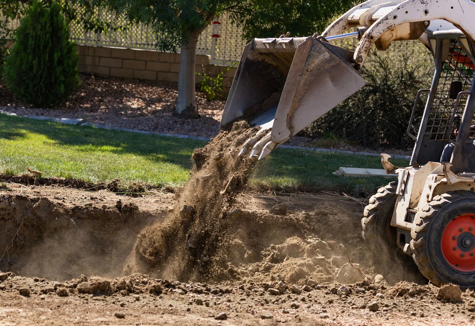Loader bucket dropping fill dirt into a pool cavity during backfill