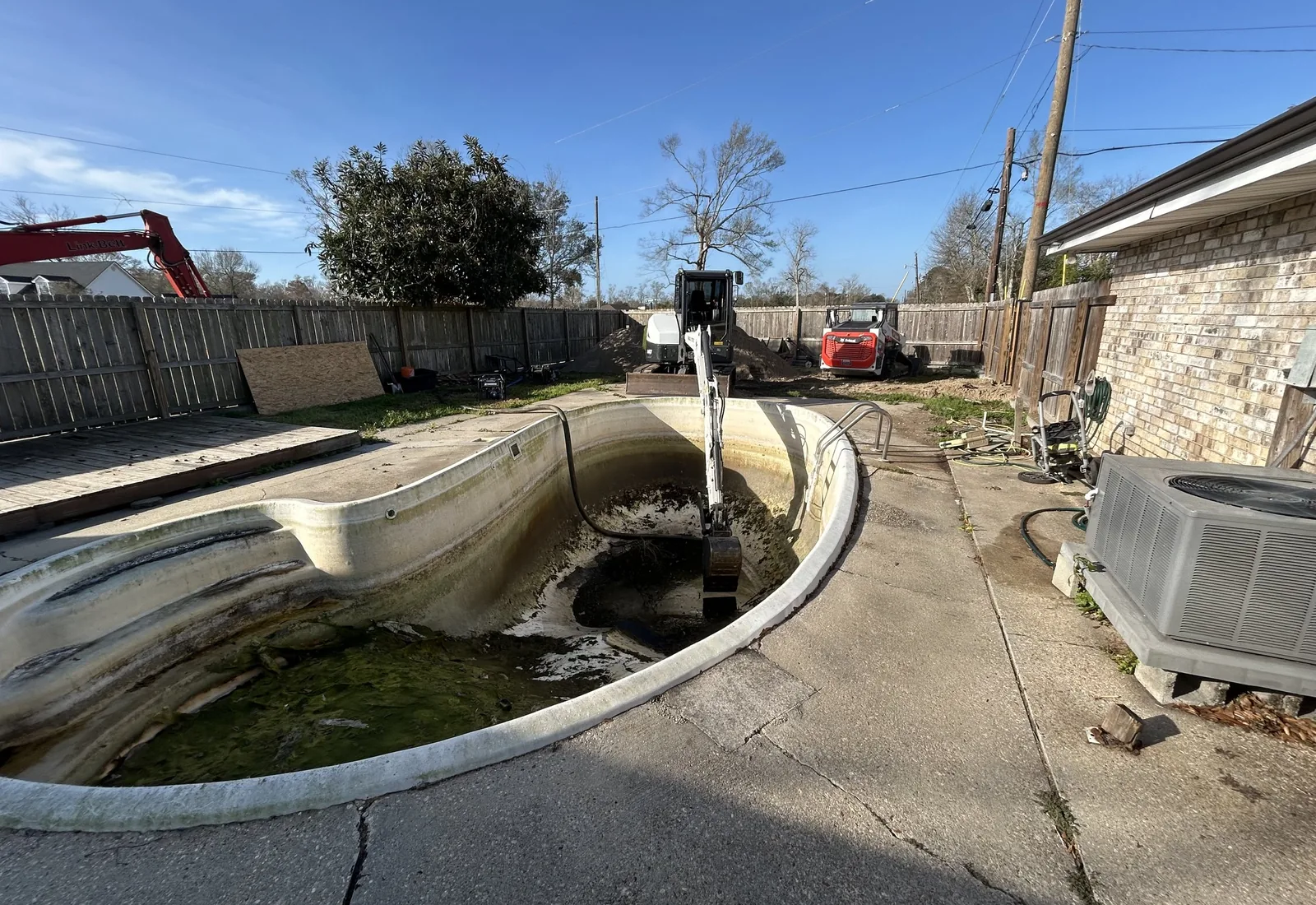 Drained swimming pool being demolished in a fenced backyard