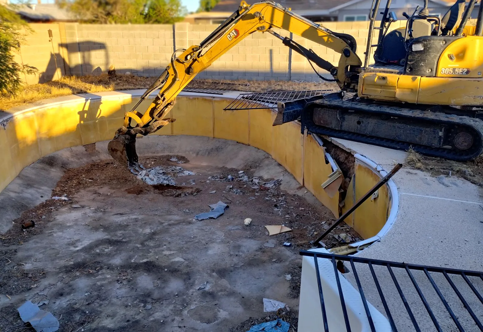 Excavator breaking up the shell of a drained backyard swimming pool