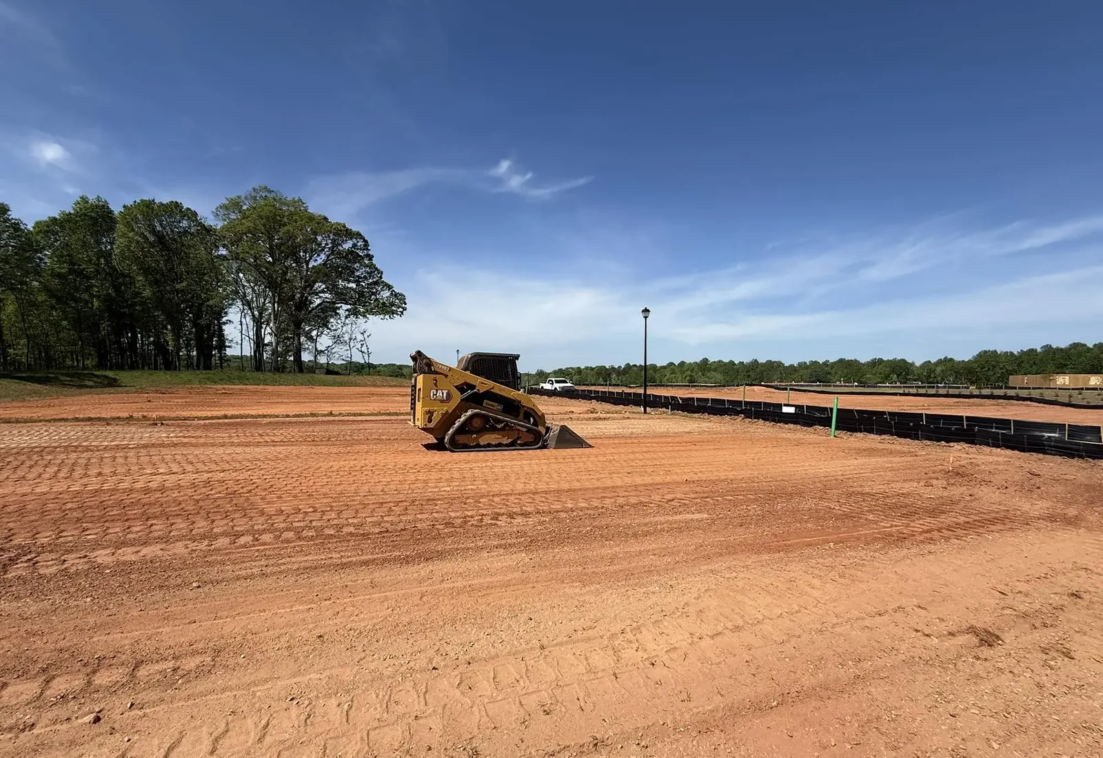 Track loader shaping a graded building pad with silt fence around it