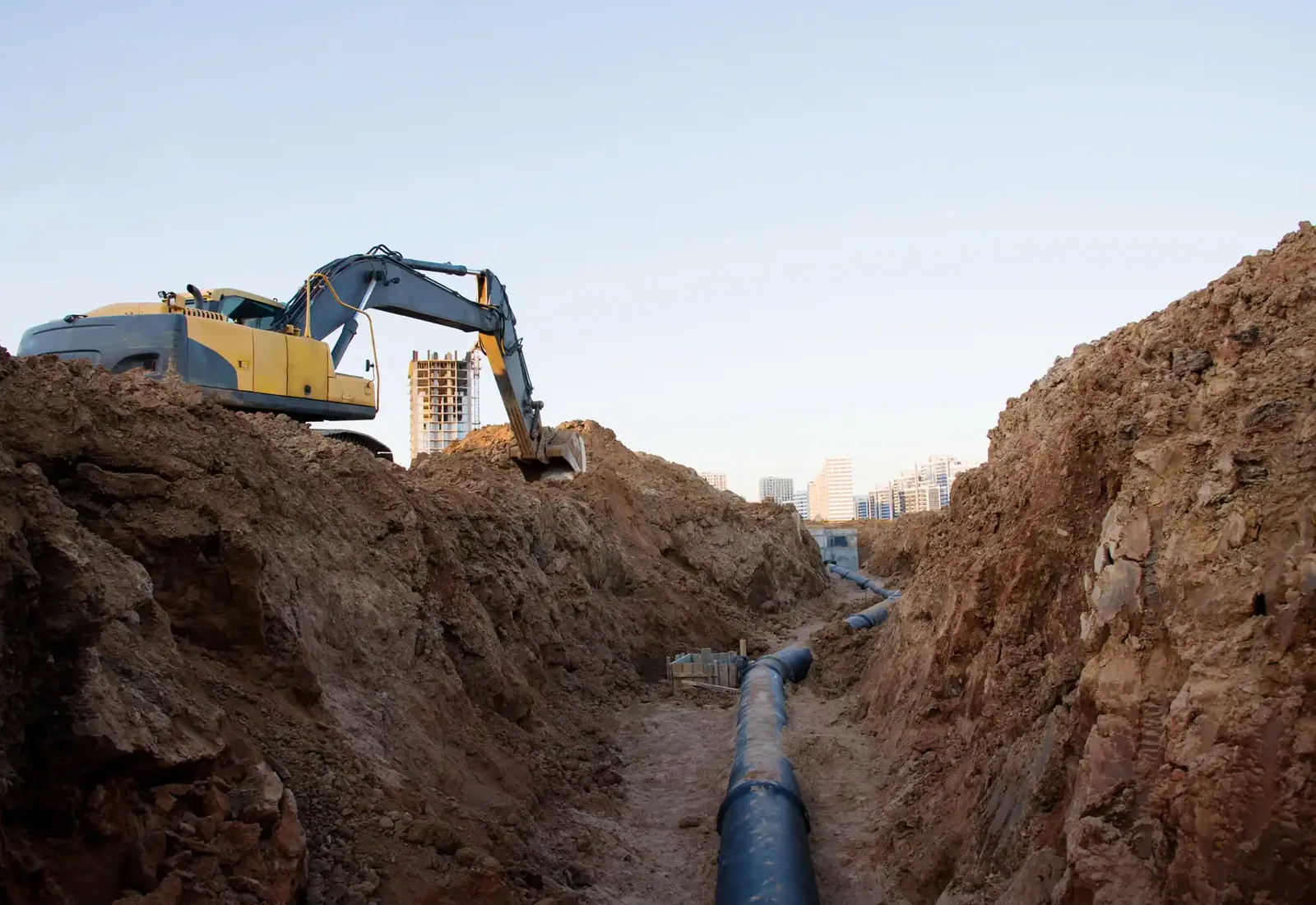 Excavator working above a long open utility trench with pipe laid in it
